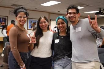 Fours students smile and pose together in a crowded room at a Horns Helping Horns event