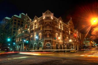 Street corner on 6th Street at night featuring a building and passing cars
